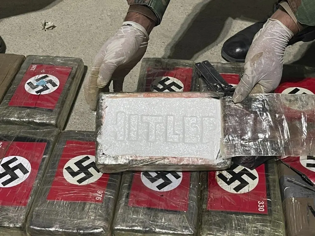 En esta imagen difundida por la Policía Antidrogas de Perú, un agente muestra paquetes de cocaína marcados con esvásticas nazis y el nombre Hitler, el jueves 25 de mayo de 2023, en el puerto de Paita, en la región de Piura, Perú. (Policía Antidrogas de P