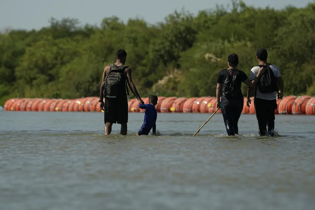 Migrantes en su ruta hacia Estados Unidos desde México camina a lo largo de las boyas instaladas como una barrera flotante sobre el río Bravo, el martes 1 de agosto de 2023, en Eagle Pass, Texas. (AP Foto/Eric Gay)