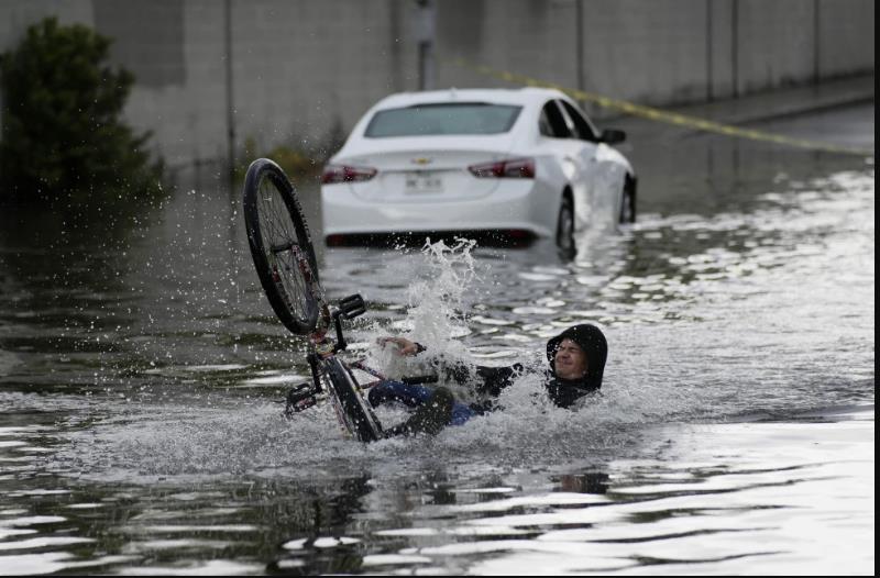 Un ciclista cae mientras intenta atravesar una calle inundada, cerca de un automóvil varado, el viernes 1 de septiembre de 2023, en Las Vegas. (Foto AP/John Locher)