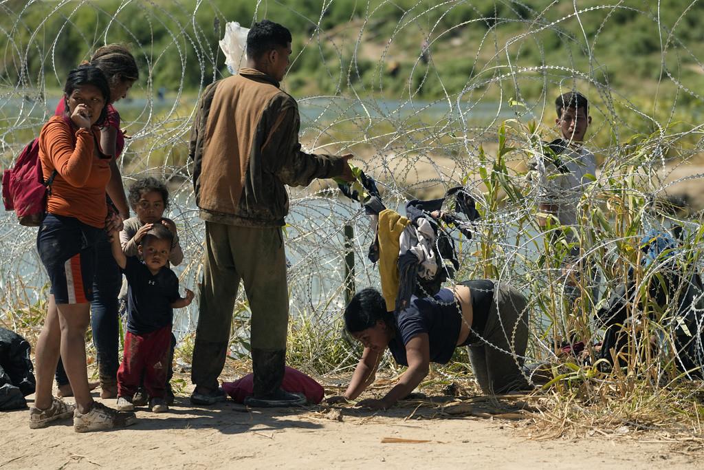 Migrantes que cruzaron a Estados Unidos desde México pasan por debajo de un alambre con cuchillas a orillas del río Bravo, el 21 de septiembre de 2023, en Eagle Pass, Texas. (AP Foto/Eric Gay)