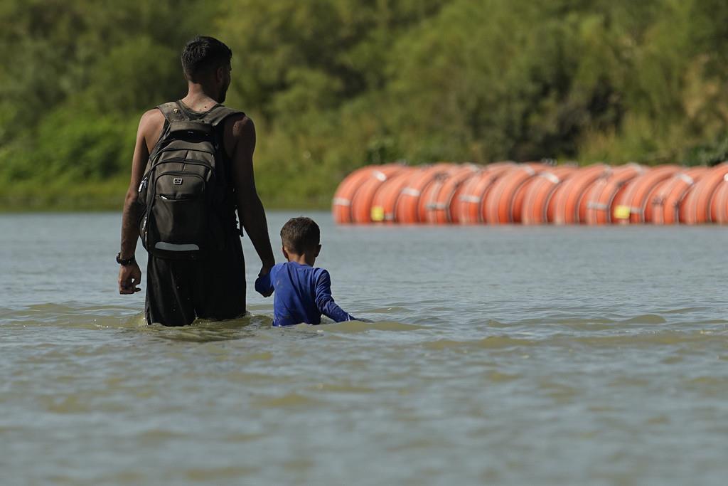 Migrantes caminan junto a grandes boyas que se utilizan como barrera fronteriza flotante en el río Bravo, el 1 de agosto de 2023, en Eagle Pass, Texas. (AP Foto/Eric Gay, Archivo)