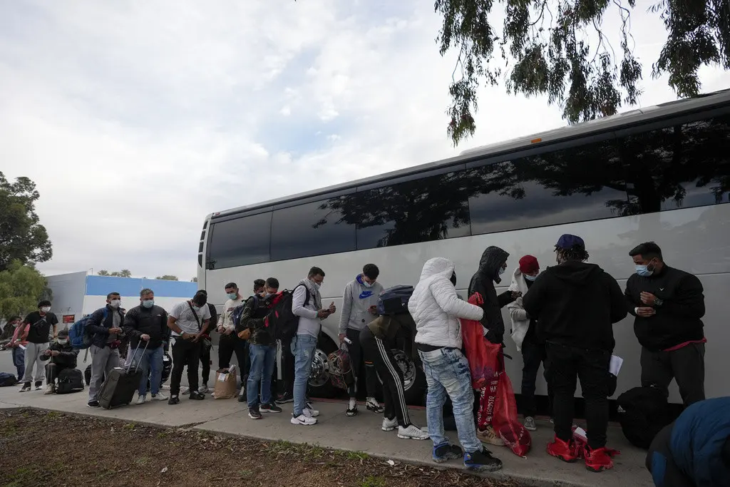 Migrantes descargan sus pertenencias de un autobús al llegar a una parada después de salir de un centro de trámites migratorios, el viernes 23 de febrero de 2024, en San Diego. (AP Foto/Gregory Bull)