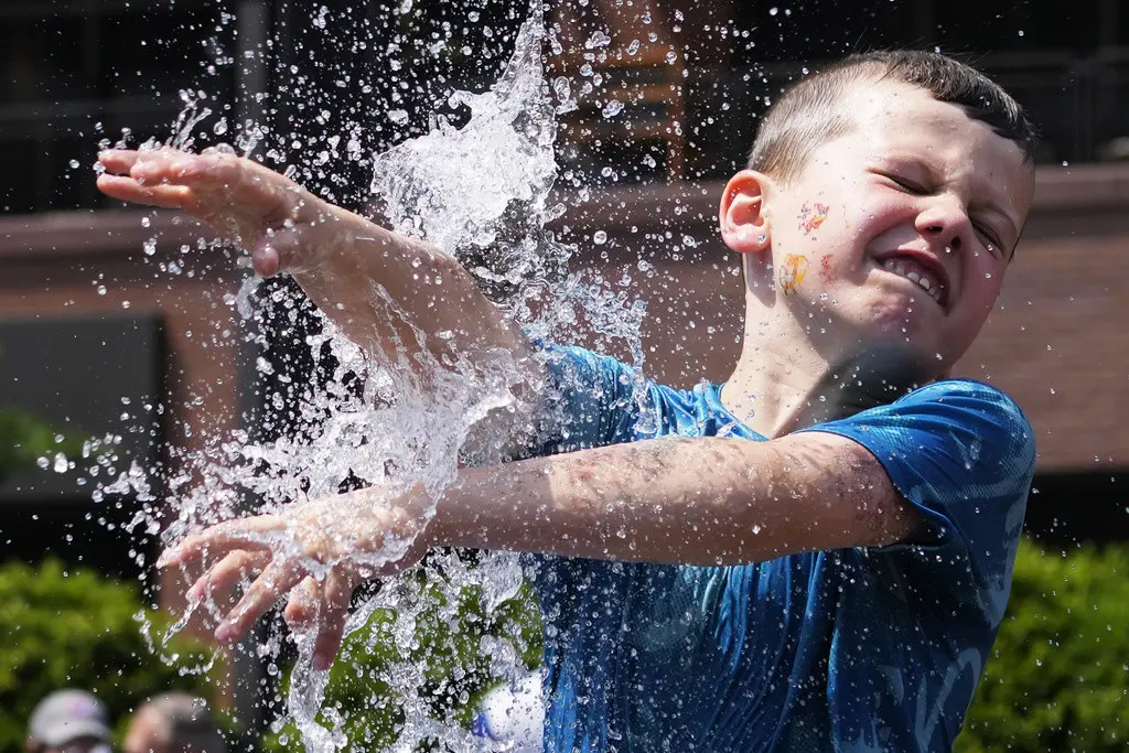 Un niño se refresca junto a una fuente junto al Wrigley Field antes de un juego de béisbol entre los Cachorros de Chicago y los Cardenales de San Luis, en unos días de tiempo cálido en la zona de Chicago, el domingo 16 de junio de 2024. (AP Foto/Nam Y. Huh