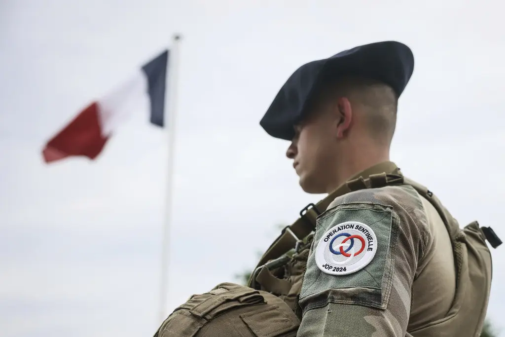 Un soldado monta guardia frente a la bandera de Francia en un campamento militar, el lunes 15 de julio de 2024, a las afueras de París. (AP Foto/Thomas Padilla)